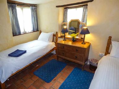A bedroom with two single beds a wooden dresser two blue lamps and checkered curtains at The Mill in Bicknoller