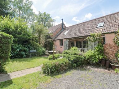 A garden with outdoor table and chairs near a stone house with tiled roof at The Barn in Bicknoller