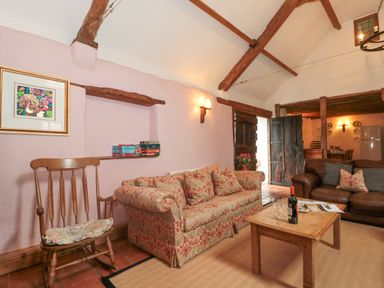 A living room with sofas a wooden rocking chair a wooden table a bottle and glasses on the table and exposed wooden beams at The Barn in Bicknoller