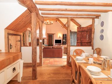 A dining area with a wooden table set for a meal and a view into a living room with exposed wooden beams at The Barn in Bicknoller