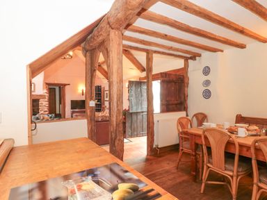 A dining area with a wooden table and chairs next to rustic wooden beams and a small opening to a living room at The Barn in Bicknoller