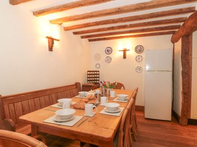 A dining room with a wooden table set with bowls cups and bread and a refrigerator in the corner at The Barn in Bicknoller