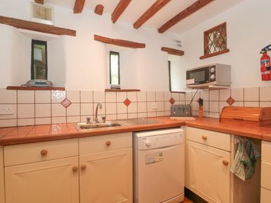 A kitchen with a sink dishwasher microwave toaster and wooden cabinets at The Barn in Bicknoller
