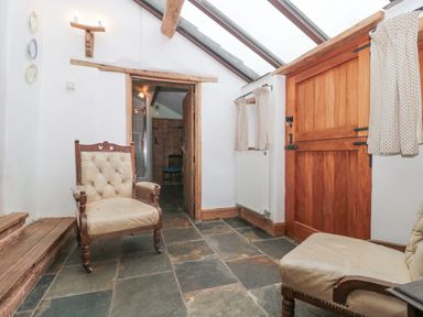 A room with two upholstered armchairs wooden door wooden steps and small windows with curtains at The Barn in Bicknoller