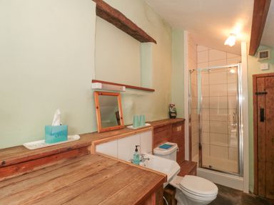A bathroom with a wooden countertop a sink a toilet a shower with glass doors and a mirror on the wall at The Barn in Bicknoller
