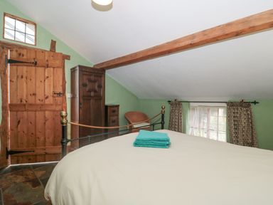 A bedroom with a bed and folded towels on it next to a wooden door wooden wardrobe and window with curtains at The Barn in Bicknoller