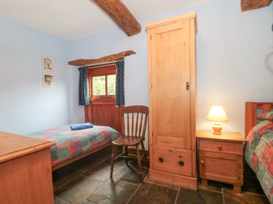 A bedroom with two beds a wooden wardrobe chair and nightstand with lamp at The Barn in Bicknoller