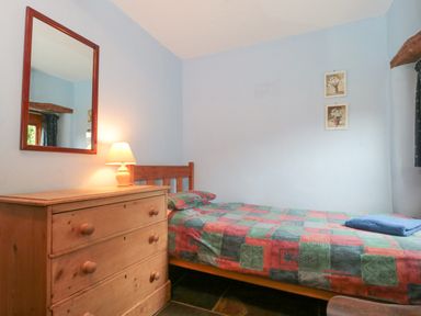 A bedroom with a wooden bed and dresser with a lamp and mirror at The Barn in Bicknoller