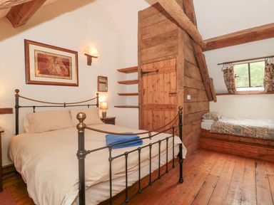 A bedroom with a double bed a single bed wooden floors and wooden beams at The Barn in Bicknoller