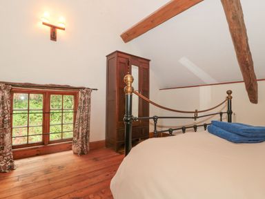 A bedroom with a metal bed frame blue towels a wooden wardrobe wooden floor and a window with floral curtains at The Barn in Bicknoller