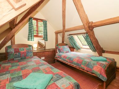 A bedroom with two single beds with colorful bedspreads and green checked curtains at The Barn in Bicknoller