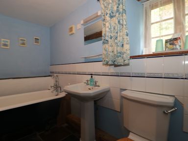 A bathroom with a bathtub sink toilet and a window with floral curtains at The Barn in Bicknoller