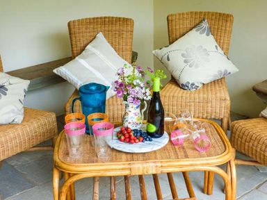 A seating area with wicker chairs cushions a table with fruit glasses a pitcher and a bottle at The Old Mill in Dolau near Llandrindod Wells