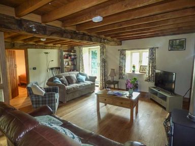 A living room with wooden ceiling beams a sofa armchair coffee table and a television at The Old Mill in Dolau near Llandrindod Wells