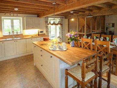 A kitchen with wooden countertops white cabinets a kitchen island with chairs and a dining table with wooden chairs at The Old Mill in Dolau near Llandrindod Wells