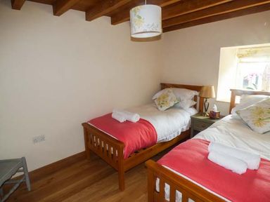 A bedroom with two single wooden beds with red throws and pillows beside a window at The Old Mill in Dolau near Llandrindod Wells