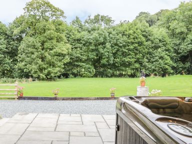 A backyard with a hot tub on a patio and a lawn with trees and potted plants at The Old Mill in Dolau near Llandrindod Wells