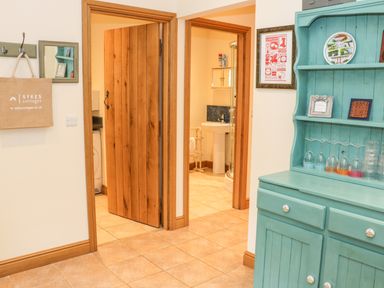 A hallway with open wooden doors showing a bathroom and a utility room and a turquoise cabinet with glasses at The Old Mill in Dolau near Llandrindod Wells