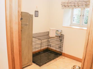 A small room with a metal dog crate a cupboard a window and a dog bowl on the floor at The Old Mill in Dolau near Llandrindod Wells