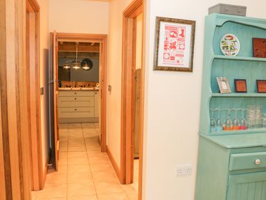 A hallway with wooden door frames leading to a kitchen with pendant lights and a turquoise cabinet with glasses and decor at The Old Mill in Dolau near Llandrindod Wells