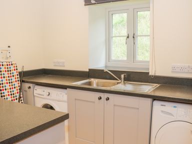 A kitchen with a double sink a window two washing machines and an ironing board at The Old Mill in Dolau near Llandrindod Wells