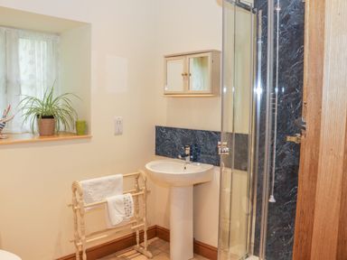 A bathroom with a pedestal sink a towel rack a window with sheer curtains and a shower area at The Old Mill in Dolau near Llandrindod Wells