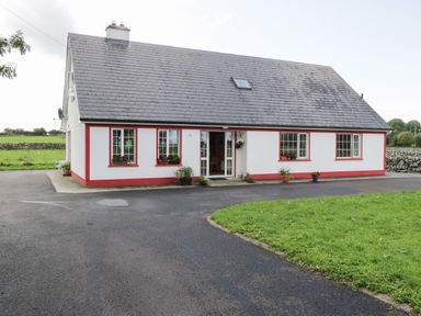 A white house with red trim surrounded by grass and a paved driveway at Lough Mask Road Fishing Lodge in Ballinrobe County Mayo