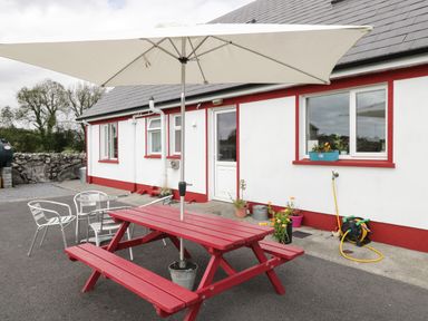 An outdoor patio with a red picnic table and white umbrella next to a white building with red trim and metal chairs at Lough Mask Road Fishing Lodge Ballinrobe County Mayo