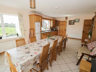 A kitchen dining area with a long table covered in a printed tablecloth and wooden chairs around it at Lough Mask Road Fishing Lodge in Ballinrobe County Mayo