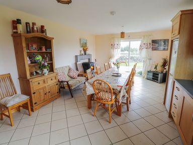 A dining area with a long table and wooden chairs a wooden cabinet a sofa a fireplace and a sliding door leading outside at Lough Mask Road Fishing Lodge Ballinrobe County Mayo