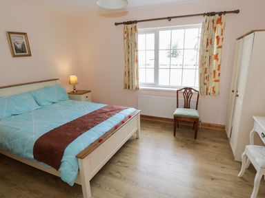 A bedroom with a bed blue bedding wooden floor chair bedside table lamp wardrobe and window with curtains at Lough Mask Road Fishing Lodge Ballinrobe County Mayo