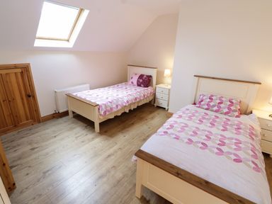 A bedroom with two single beds with pink and white bedding and bedside tables with lamps at Lough Mask Road Fishing Lodge Ballinrobe County Mayo