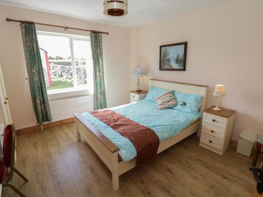 A bedroom with a bed blue bedding and red throw next to two bedside tables with lamps and a window with green curtains at Lough Mask Road Fishing Lodge in Ballinrobe County Mayo