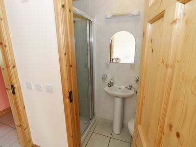 A bathroom with a shower cubicle a pedestal sink a mirror and wooden doors at Lough Mask Road Fishing Lodge in Ballinrobe County Mayo