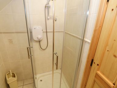 A shower area with tiled walls a glass door a shower unit and a small trash bin at Lough Mask Road Fishing Lodge Ballinrobe County Mayo