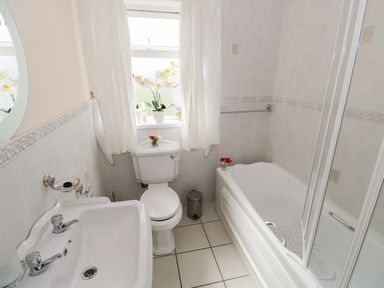 A bathroom with a bathtub shower, toilet, sink, window with curtains and floral decorations at Lough Mask Road Fishing Lodge Ballinrobe County Mayo