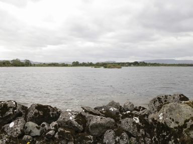 A rocky shoreline with water and distant trees and hills at Lough Mask Road Fishing Lodge in Ballinrobe County Mayo