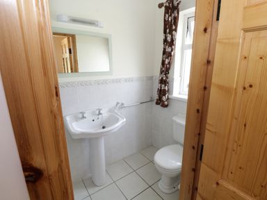 A small bathroom with a pedestal sink a toilet a mirror and a window with floral curtains at Lough Mask Road Fishing Lodge in Ballinrobe County Mayo