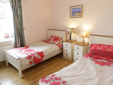 A bedroom with two single beds with floral bedding two bedside tables with lamps and a window with curtains at Lough Mask Road Fishing Lodge in Ballinrobe County Mayo