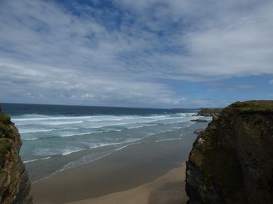 A sandy beach with waves and cliffs on both sides at Spindrift in Porth near Newquay