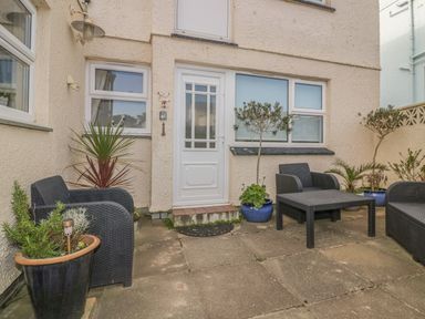 An outdoor patio with black wicker chairs and table and potted plants at Spindrift in Porth near Newquay
