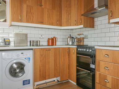 A kitchen with wooden cabinets a washing machine an electric kettle and a black oven at Spindrift in Porth near Newquay