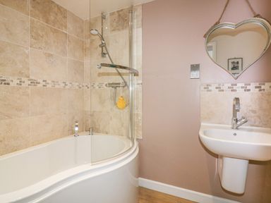 A bathroom with a curved bathtub and shower and a white sink with a heart shaped mirror on the wall at Spindrift in Porth near Newquay