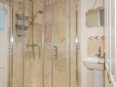 A bathroom with a glass shower enclosure a showerhead a wall mirror a pedestal sink and a towel rack at Spindrift in Porth near Newquay
