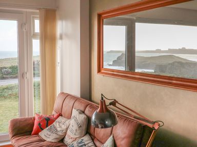 A living room with a sofa near a window showing a coastal view at Spindrift in Porth near Newquay