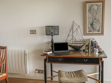 A desk with a laptop lamp decorative boat books and a mug with a stool in front at Spindrift in Porth near Newquay