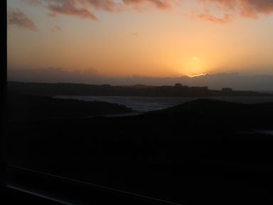A sunset over a coastal landscape with hills and water at Spindrift in Porth near Newquay