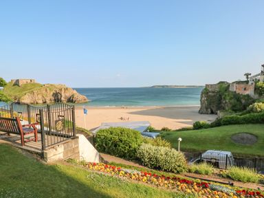 A beach view with a sandy shore ocean a bench a gate flowers and green grass at Berlin House in Tenby