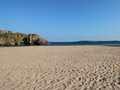 A sandy beach with rock formations and buildings near the shore with the sea and a clear sky at Berlin House in Tenby