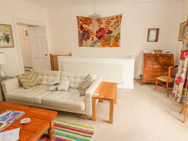A living room with a white sofa a wooden coffee table a striped rug and a wooden desk at Berlin House in Tenby